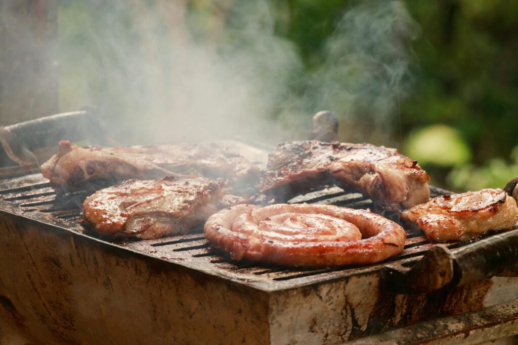 A sizzling BBQ grill with meat and sausages smoking outdoors, perfect for summer cookouts.